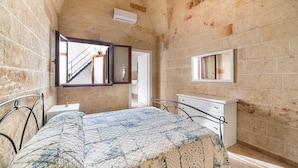 A bedroom with a bed, a bedside table, a dresser, a window, and a staircase visible through an open door. - Casetta Annarosa (San Pancrazio Salentino)