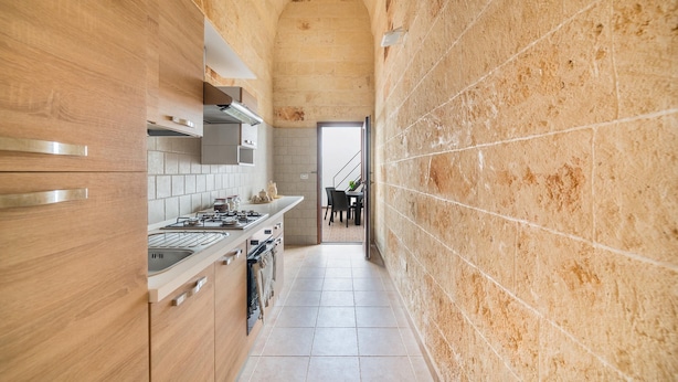 A narrow kitchen with wooden cabinets, a stainless steel range hood, and a tiled backsplash. - Casetta Annarosa (San Pancrazio Salentino)