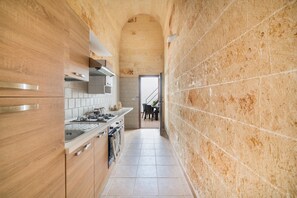 A narrow kitchen with wooden cabinets, a stainless steel range hood, and a tiled backsplash. - Casetta Annarosa (San Pancrazio Salentino)