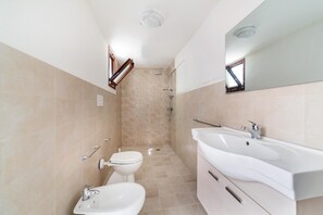 A modern bathroom with a toilet, bidet, sink, and shower.