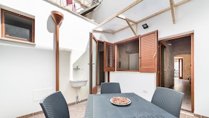 A dining area with a table and chairs, a bowl of snacks, a window, and a sink. - Casetta Annarosa (San Pancrazio Salentino)