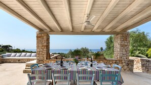 An outdoor dining area with stone pillars, a wooden ceiling, and a view of the sea. - Villa Rio (Patu)