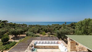 A rooftop terrace with a stone wall, a white sofa, and a view of the sea and olive trees. - Villa Rio (Patu)