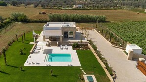 Una casa moderna con piscina, mobiliario exterior y un viñedo al fondo.