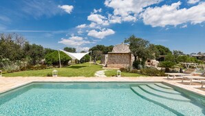 A clear swimming pool with a stone structure in the background, surrounded by greenery and a clear sky. - Villa Elaion (Salve)