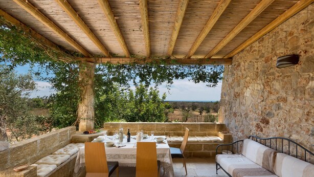 An outdoor patio with stone walls, a wooden ceiling, and a view of the countryside. - Villa Elaion (Salve)