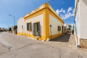 A narrow street with a yellow building featuring a small entrance and a blue sign. - Casa Giusy (Gagliano del Capo)
