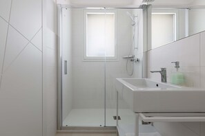 Uma casa de banho moderna com chuveiro envolto em vidro, lavatório branco e espelho.