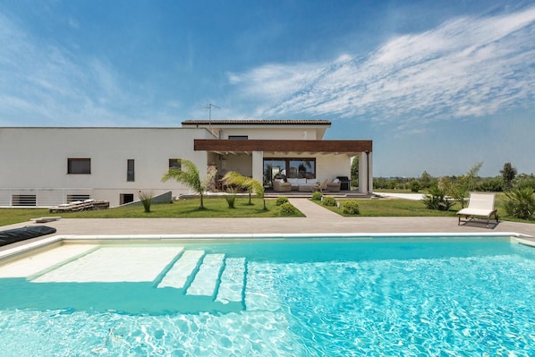 A modern house with a swimming pool, a patio, and a well-maintained lawn.