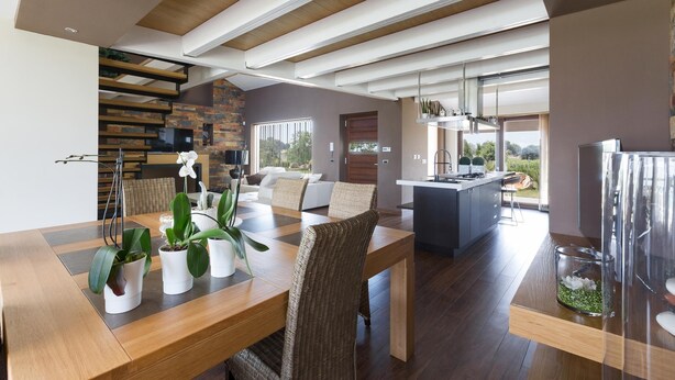 Una cocina moderna con una isla central, suelo de madera y un comedor con mesa y sillas de madera.