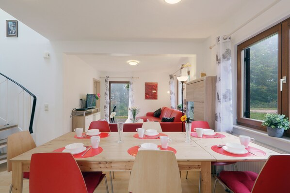 Un coin repas avec une table en bois dressée pour quatre personnes, des chaises rouges et un canapé rouge en arrière-plan.