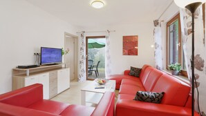 Un salon moderne avec un canapé rouge, une table basse blanche et un téléviseur à écran plat posé sur un meuble en bois.