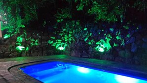 Una piscina con un muro de piedra y follaje verde al fondo.