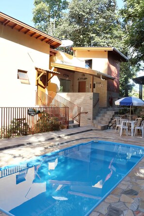 A swimming pool with a clear blue water surface, surrounded by stone tiles. There is a wooden fence and a staircase leading to a building with a sign that reads "Piscina Profissional 1,40m". - Pousada Mirante do Lago (Lindoia)