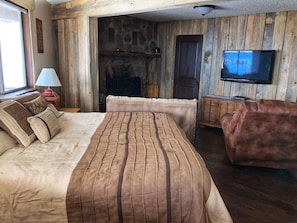 Een gezellige kamer met een groot bed, een houten wand, een televisie en een open haard.