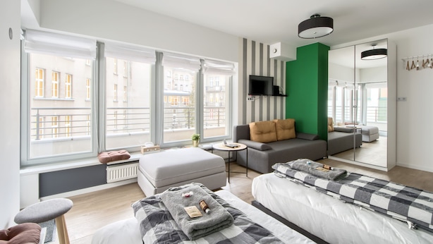 A modern hotel room with large windows, a sofa, a bed, and a TV.