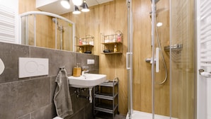 A modern bathroom with a shower, a sink, and a mirror. There are shelves with toiletries and a towel hanging on the wall.