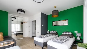 A modern bedroom with two beds, a green accent wall, and a large mirror.