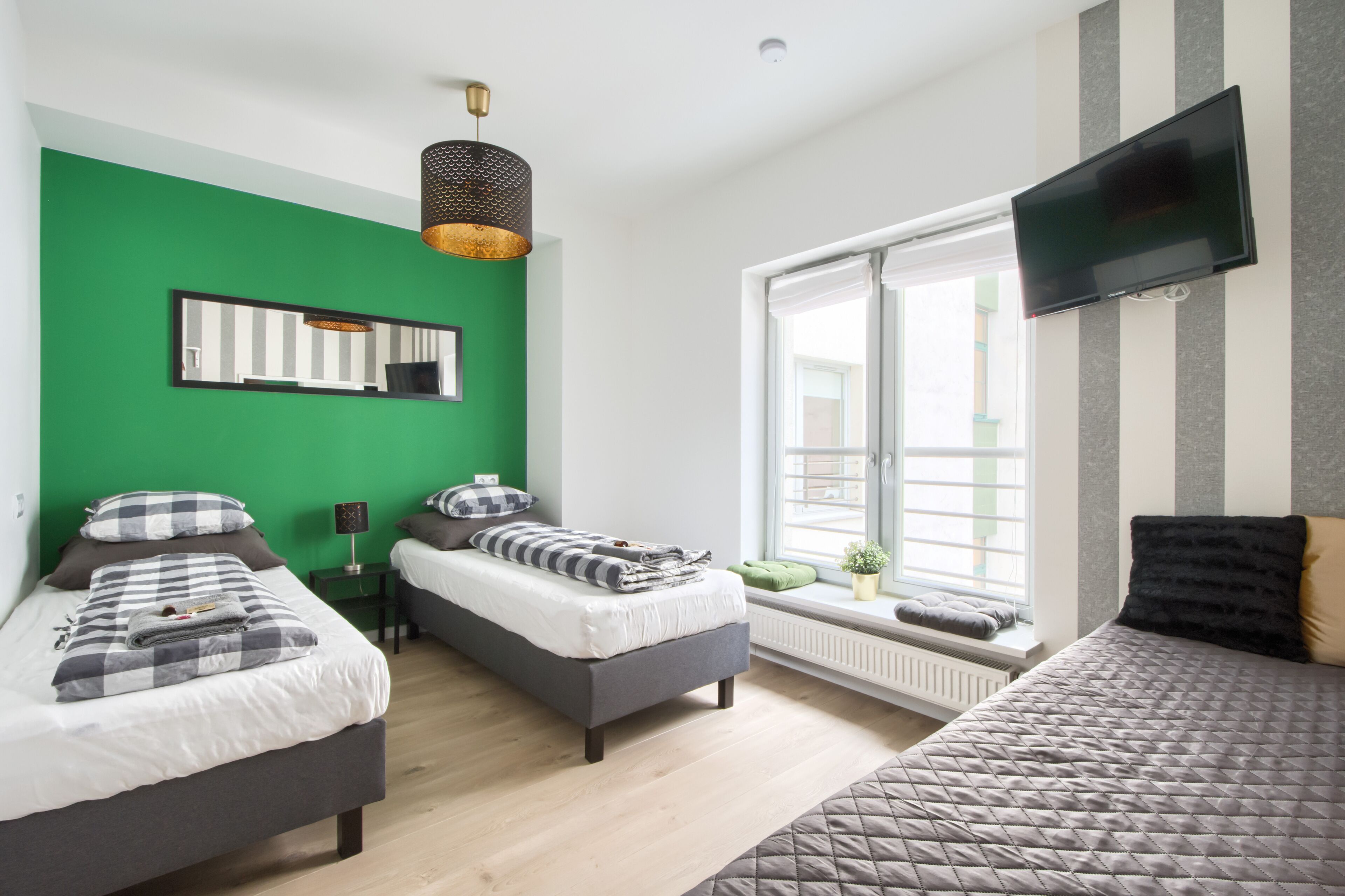 Une chambre avec deux lits, une grande fenêtre, un téléviseur à écran plat et un mur d’accent de couleur verte.