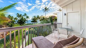 A balcony with a view of palm trees and the ocean, a table with chairs, and a sofa.