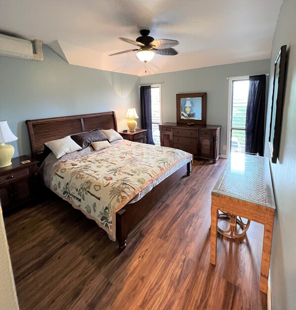 A bedroom with a wooden bed, a nightstand, a dresser, a ceiling fan, and a window with curtains.