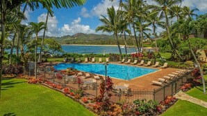 A pool area with lounge chairs, surrounded by palm trees and a view of the ocean.