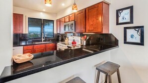 A modern kitchen with dark countertops, wooden cabinets, stainless steel appliances, and pendant lighting.