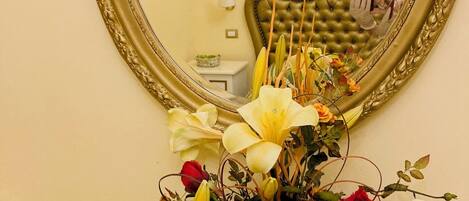 A mirror with an ornate gold frame, a floral arrangement in a vase, and a bed with striped bedding.