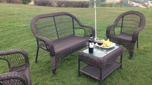 Un coin salon extérieur en osier, avec deux chaises et une table, une bouteille de vin et un verre de vin rouge.