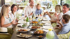 Un groupe de personnes est assis à la terrasse d’un restaurant, et différentes assiettes et boissons sont disposées sur la table.