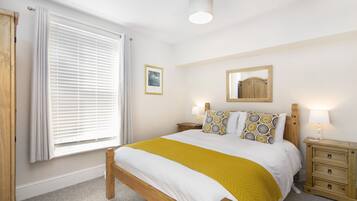 A bedroom with a bed, a nightstand, a dresser, a window with blinds, and a ceiling light.