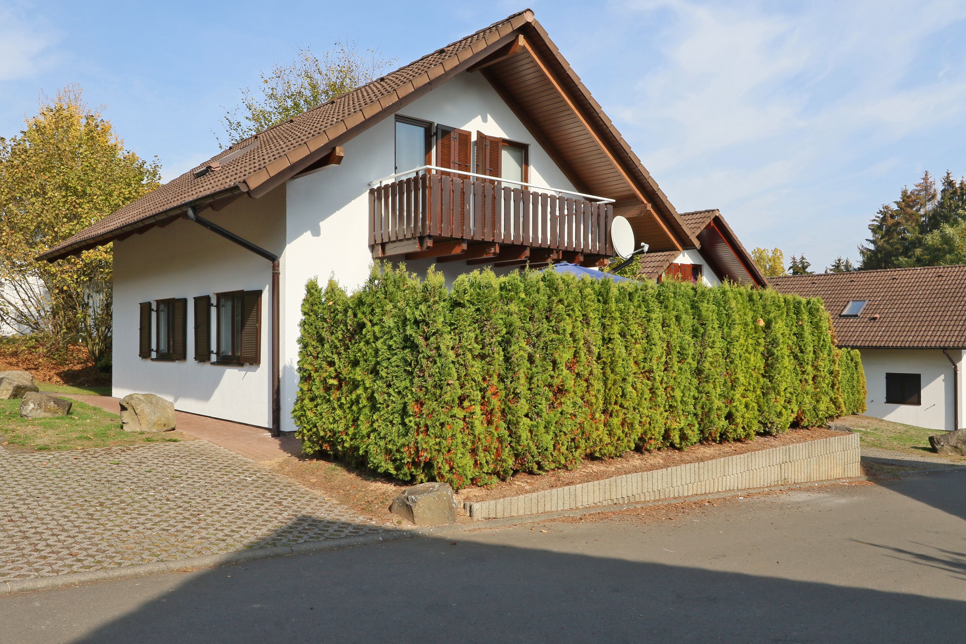 A two-story house with a balcony, a satellite dish, and a well-maintained hedge.