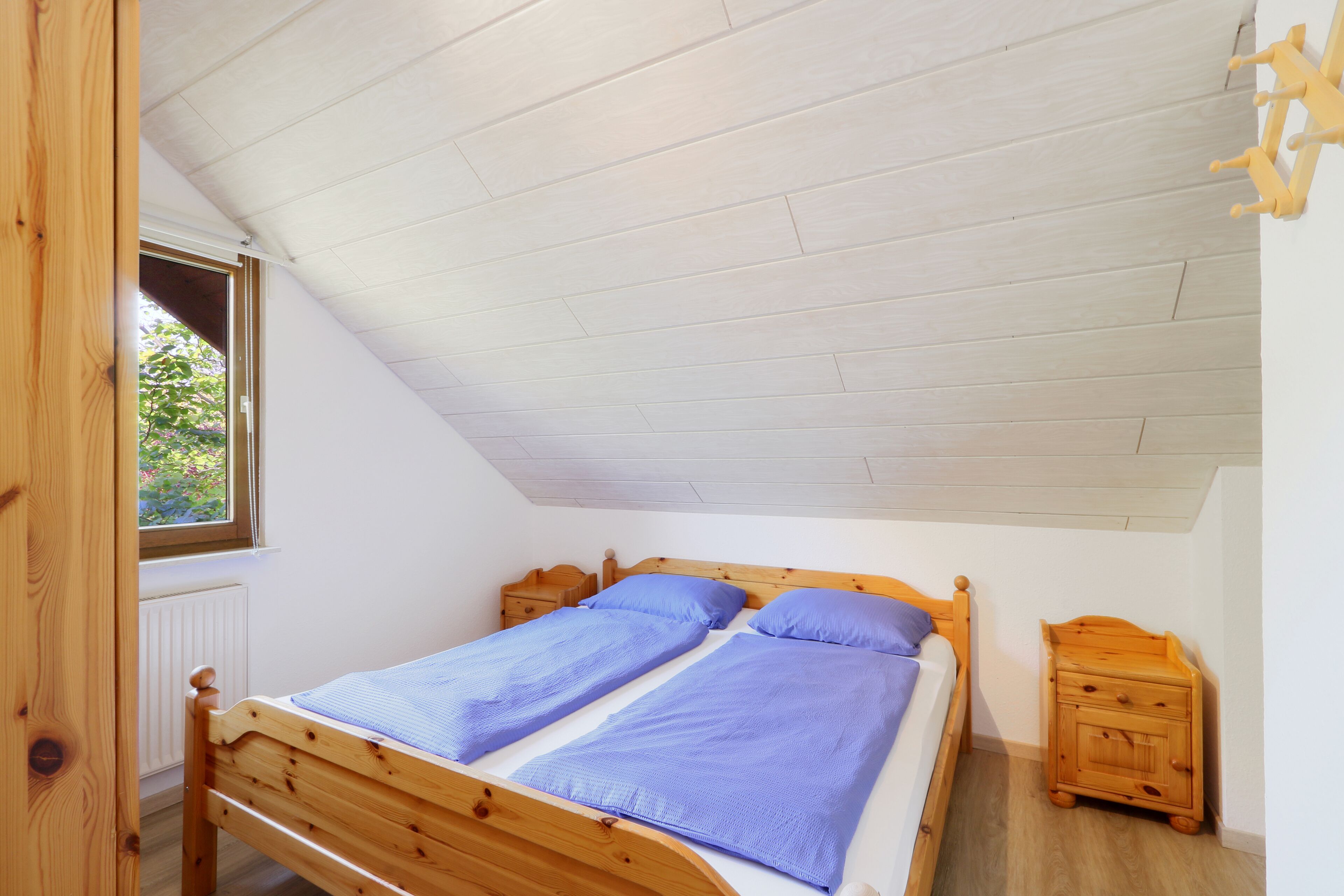 A bedroom with a wooden bed, two nightstands, a window, and a sloped ceiling.