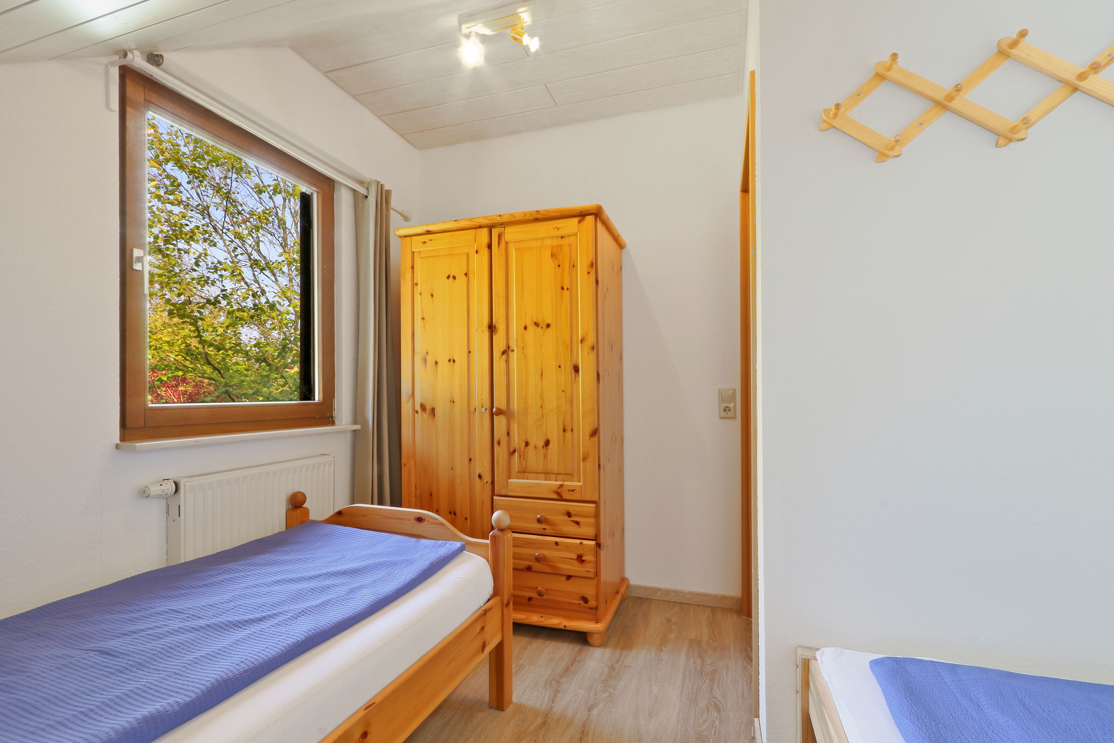 Ein Schlafzimmer mit einem Holzschrank, einem Bett mit blauer Matratze und einem Fenster mit Blick auf Bäume.