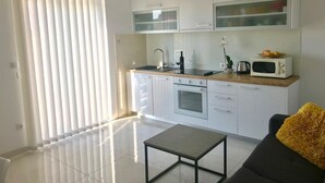 Eine moderne Küche mit weißen Schränken, einer Mikrowelle und einem Spülbecken. Es gibt einen Esstisch und ein Sofa mit einem gelben Kissen.
