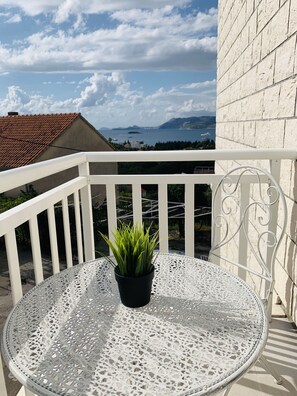 A white metal table with a potted plant on a balcony with white railings and a view of the sea and mountains. - Apartments Dupcic Cavtat (Konavle)