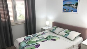 Ein ordentlich bezogenes Bett mit Kakteendecke, eine Nachttischlampe und ein Gemälde einer Küstenlandschaft an der Wand.