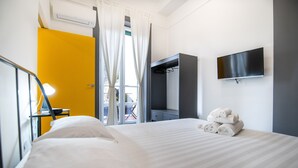 A hotel room with a bed, a TV mounted on the wall, a wardrobe, and a window with curtains. - Salerno 1950 (Salerno)