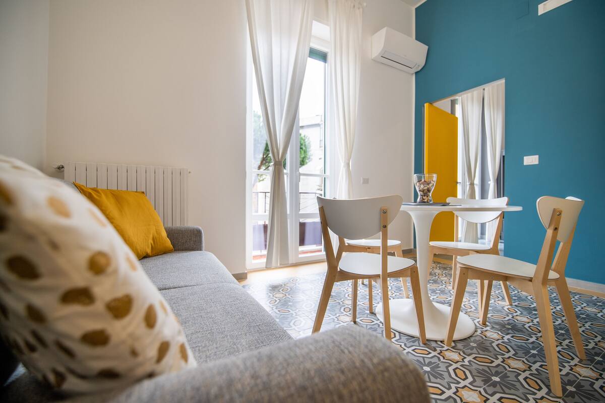 Uma sala de estar moderna com um sofá, cadeiras, uma mesinha e uma janela com cortinas.