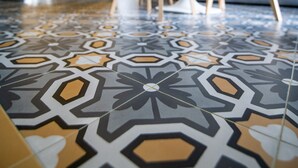 A dining area with a round table and chairs, a yellow cabinet, and patterned floor tiles. - Salerno 1950 (Salerno)