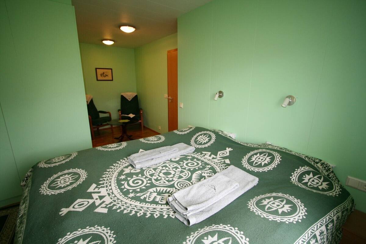 Ein Zimmer mit einem Bett, zwei Stühlen, einer Tür und einer Wandleuchte.