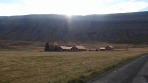 A rural property with a farmhouse and outbuildings, surrounded by open fields and a mountain backdrop. - Skarð (Fjardabyggd)