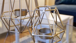Dois castiçais metálicos geométricos sobre uma mesa de vidro.