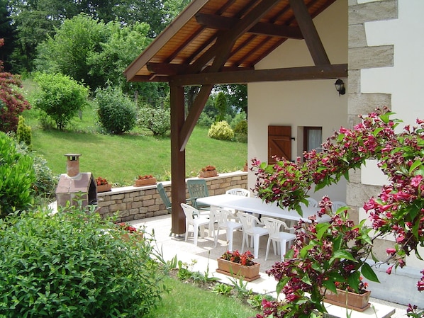 A covered patio with a table and chairs, surrounded by potted plants and a stone wall.