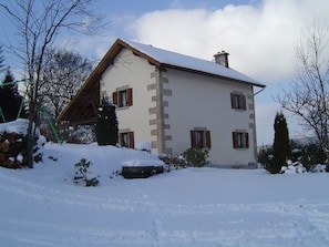 A snow-covered two-story house with a sloped roof and wooden beams.