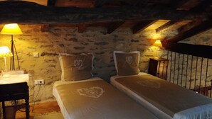Una habitación acogedora con dos camas, una pared de piedra, vigas de madera y dos lámparas de noche.