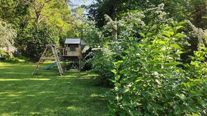 Una casita de juegos de madera con un tobogán y una escalera de escalada en un jardín exuberante.