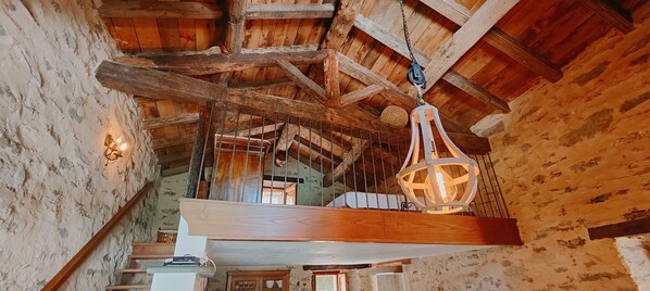 A rustic interior with exposed wooden beams, a hanging light fixture, and a staircase leading to an upper level.