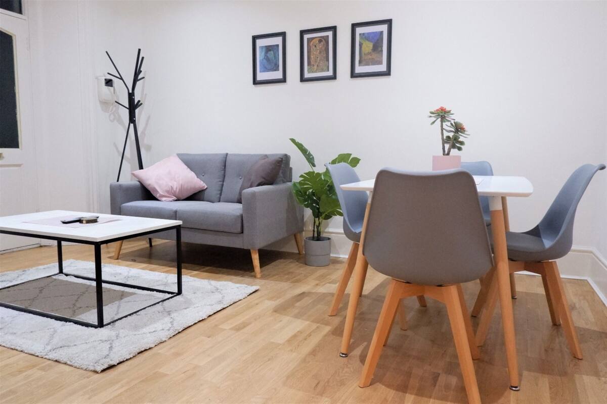 Un salon moderne avec un canapé gris, une table basse blanche et un coin repas comprenant une petite table et des chaises bleues.