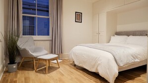 Une chambre à coucher avec un lit, une chaise, une plante en pot et une fenêtre avec des rideaux.